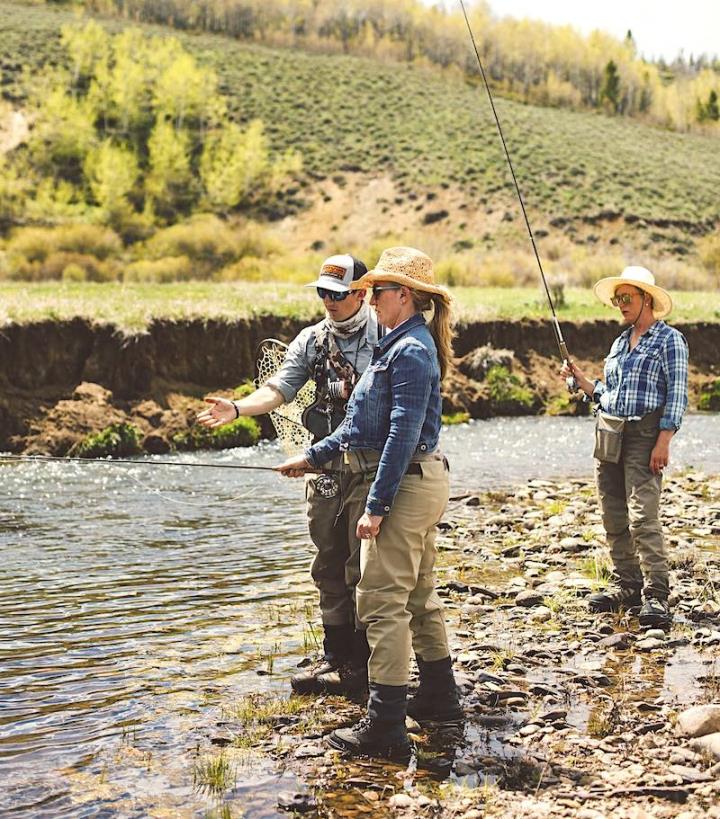 Three people standing by a river in fishing gear on a sunny day