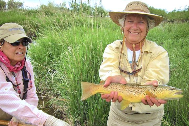 Two people wearing hats next to grassy hill one holding a fish