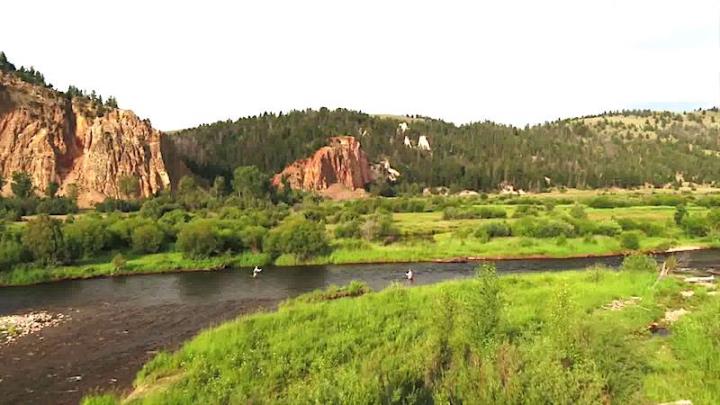 Aerial shot of brown river green grassy banks and two people fishing