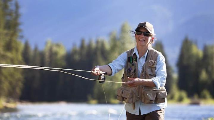 Smiling person in cap and sunglasses casting fishing line under blue sky