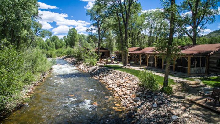 Brown cabins next to river blue sky with clouds