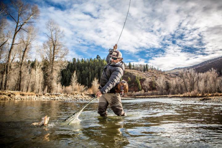 Person in hat and sunglasses standing in water casting a fishing rod